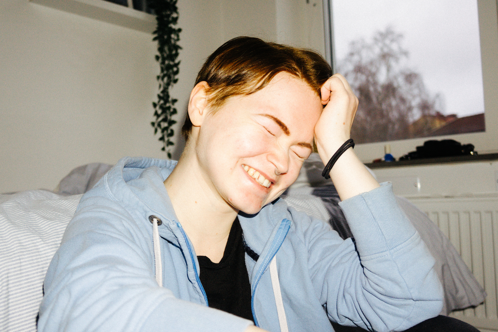 Person som blundar. Hen kan tolkas se glad, ledsen eller förlägen ut.